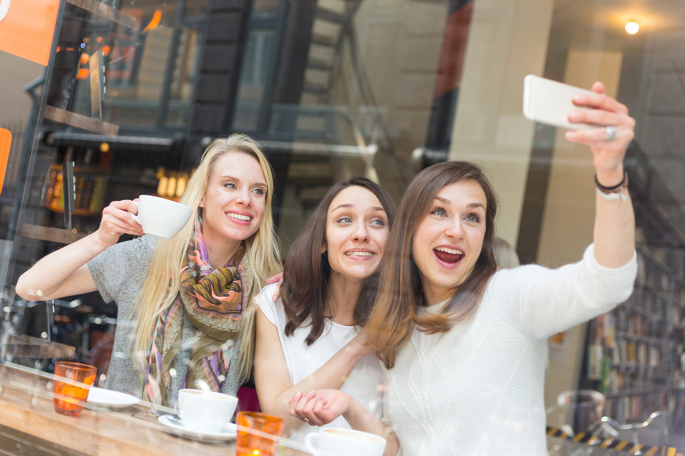 Three middle-aged, attractive, well-styled white women taking a group selfie and posing in a coffeeshop, Getty Images