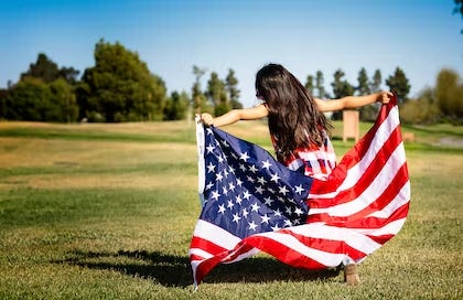 Young girl holding an American flag in a park, symbolizing patriotism and hope for the future.