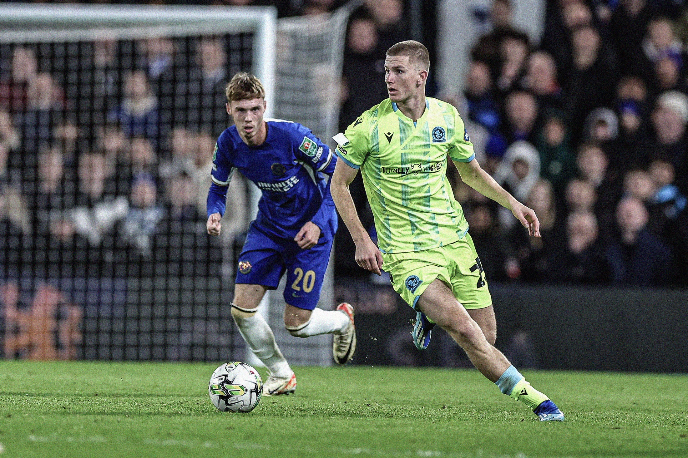 A photo of Adam Wharton playing for Blackburn Rovers against Chelsea wearing a highlighter yellow kit. In the background is Chelsea's Cole Palmer.