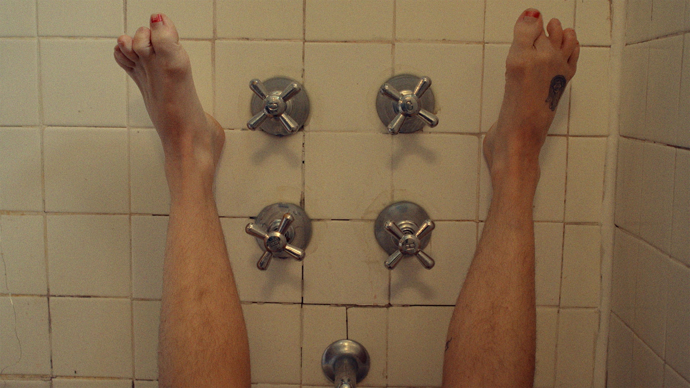 A woman's feet propped up against the wall of a bathroom, with her toes clenching