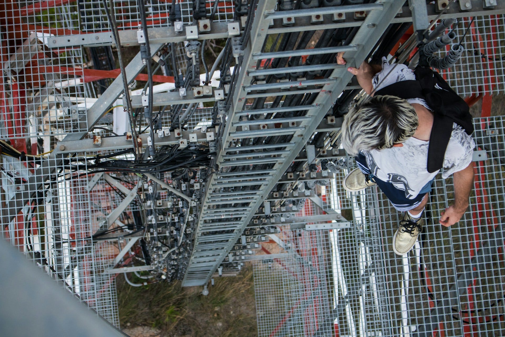 A man stands on the edge of a high platform about to step onto a ladder that leads to the ground.