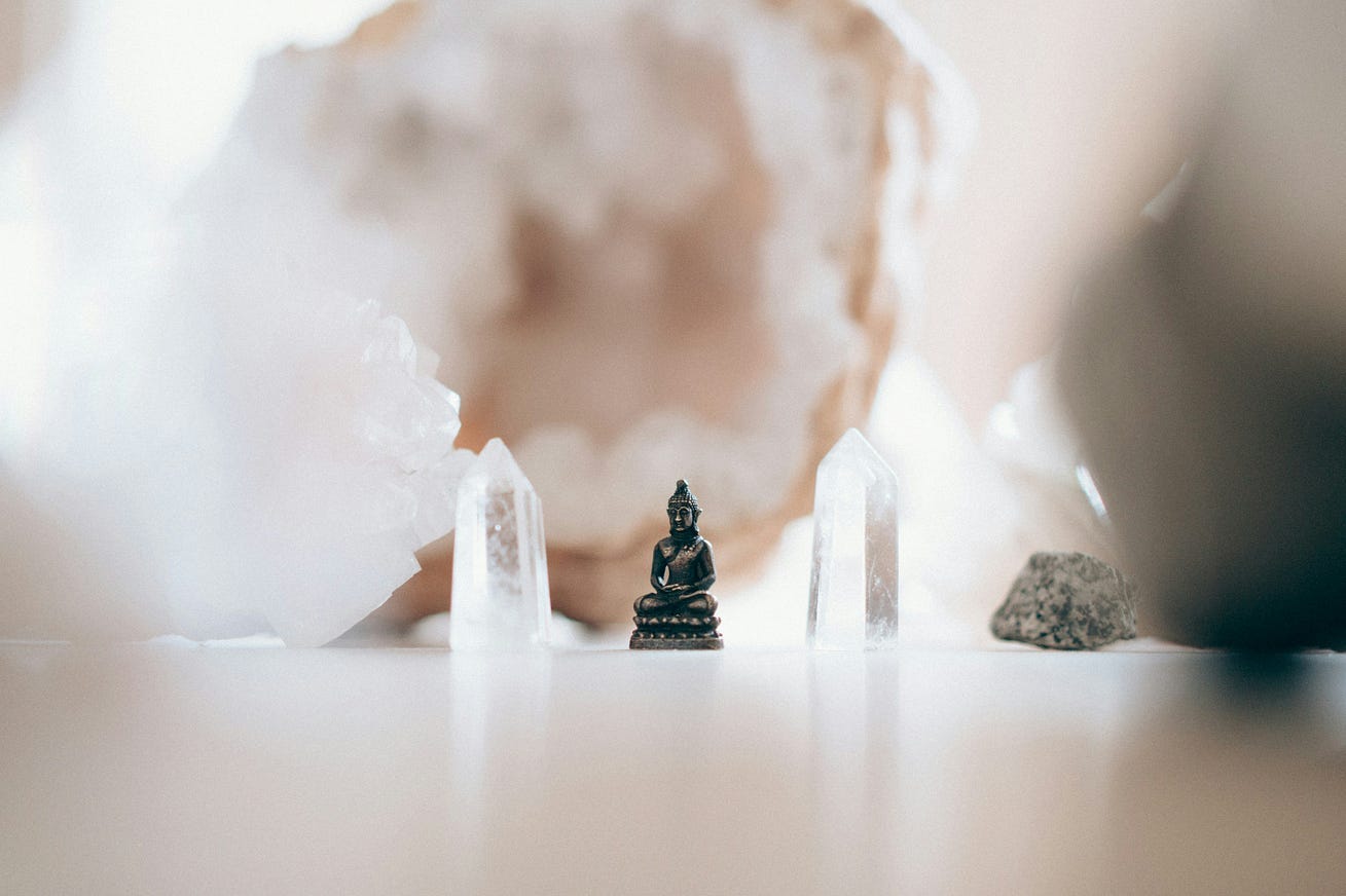 2 crystals, buddha statue and clump of mineral with blurred background