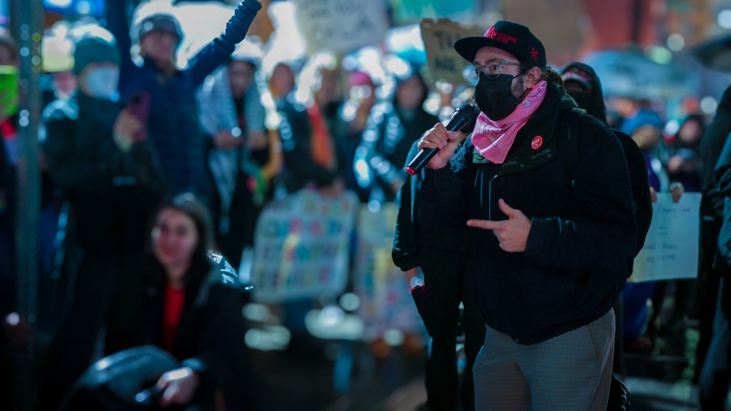 Joe Holldendoner holds a microphone as he speaks to a blurred crowd of protestors