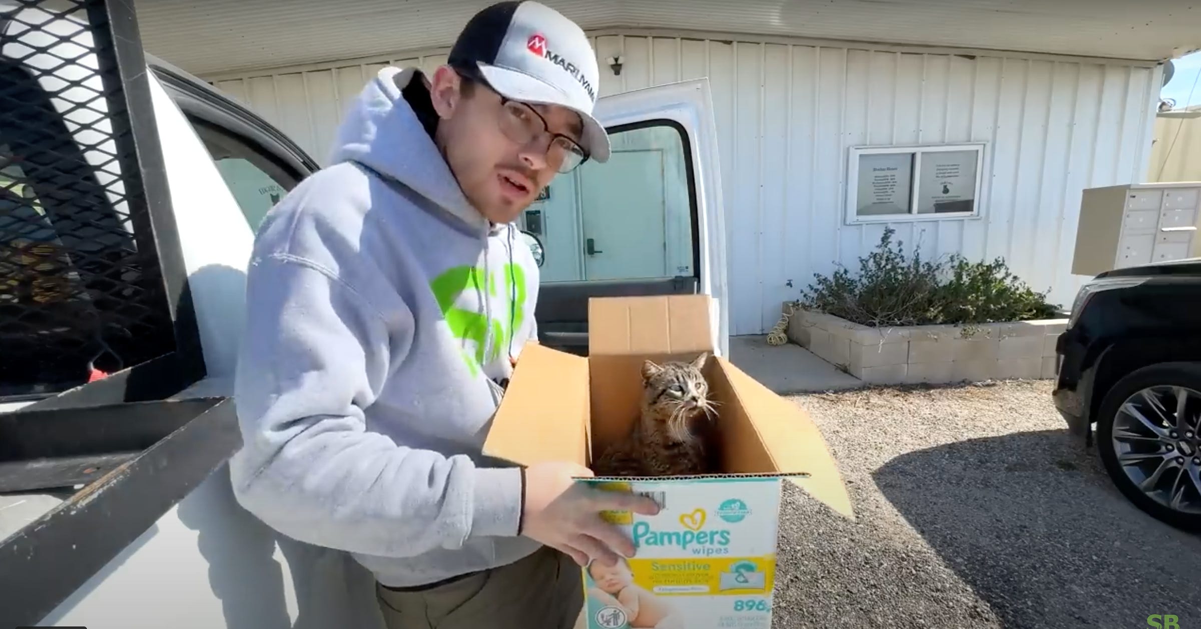Spencer B. of SB Mowing stands in front of Edgar & Ivy's Cat Sanctuary holding a cat in a box in his hands.