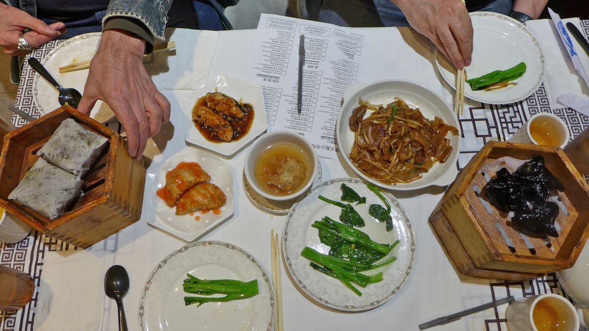 A table with several plates and steamers, and a few hands.