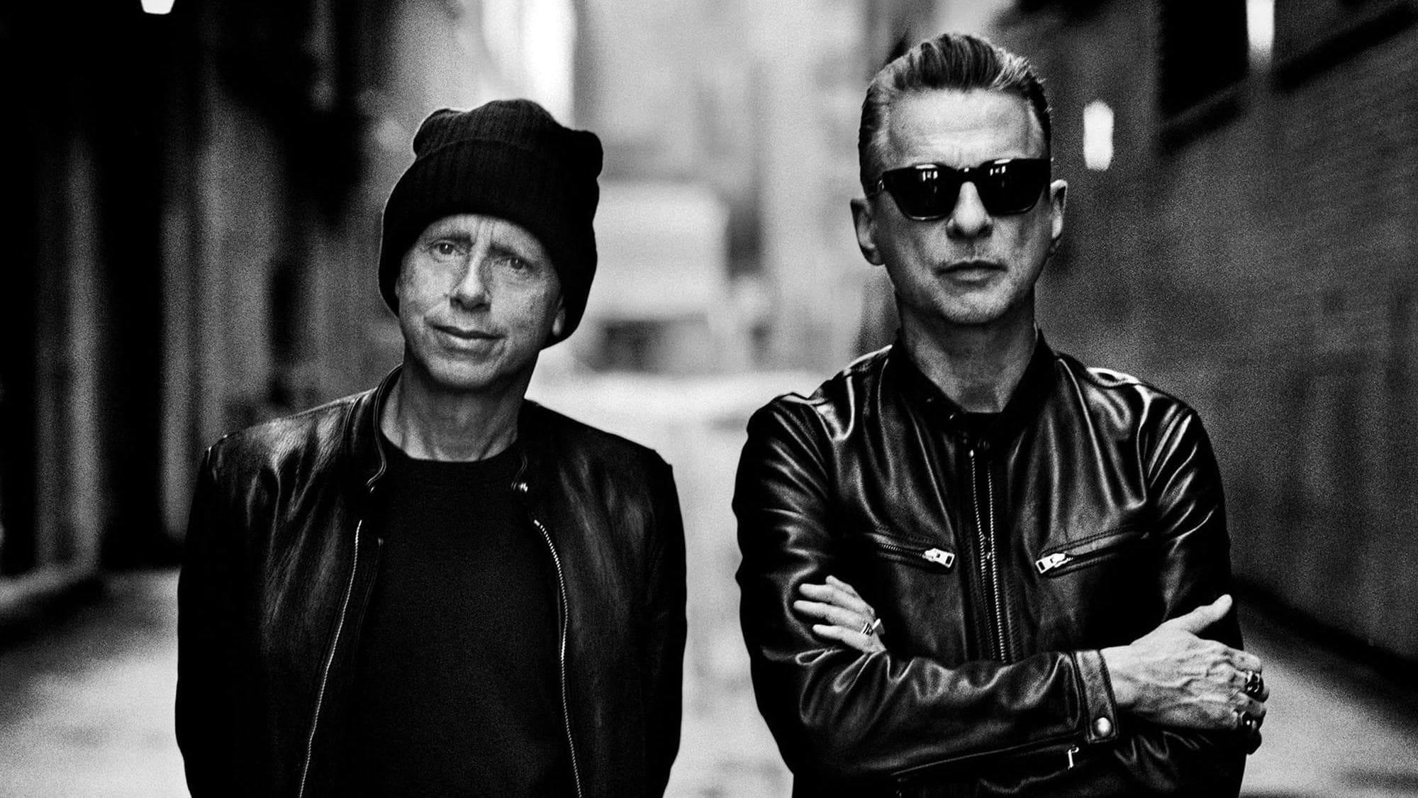 A black-and-white photo of Depeche Mode's Martin Gore and David Gahan standing on a street with an out-of-focus background