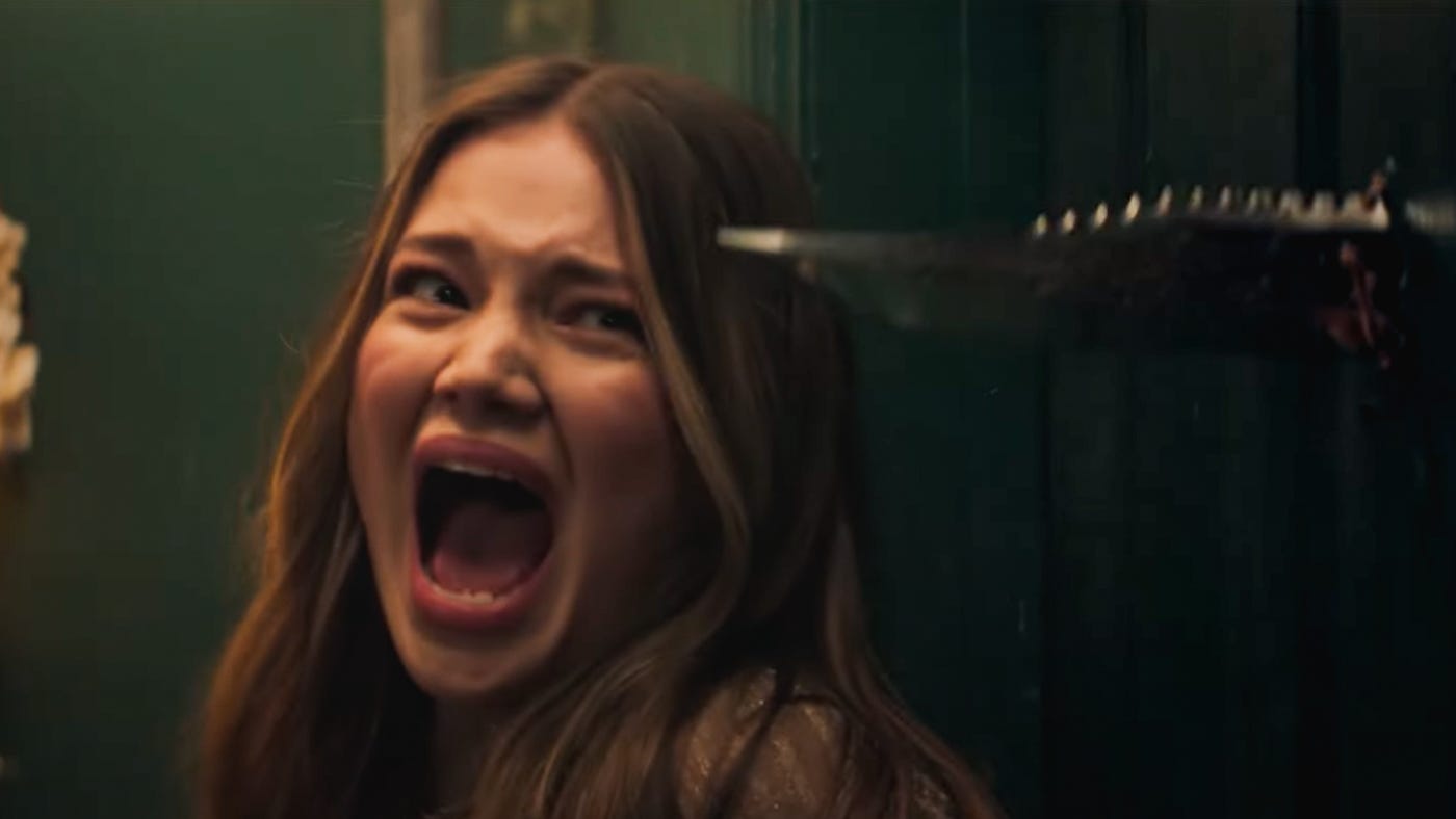 Olivia Holt screams as a large serrated blade in the foreground bursts through a door beside her. Olivia Holt screams as a large serrated blade in the foreground bursts through a door beside her.