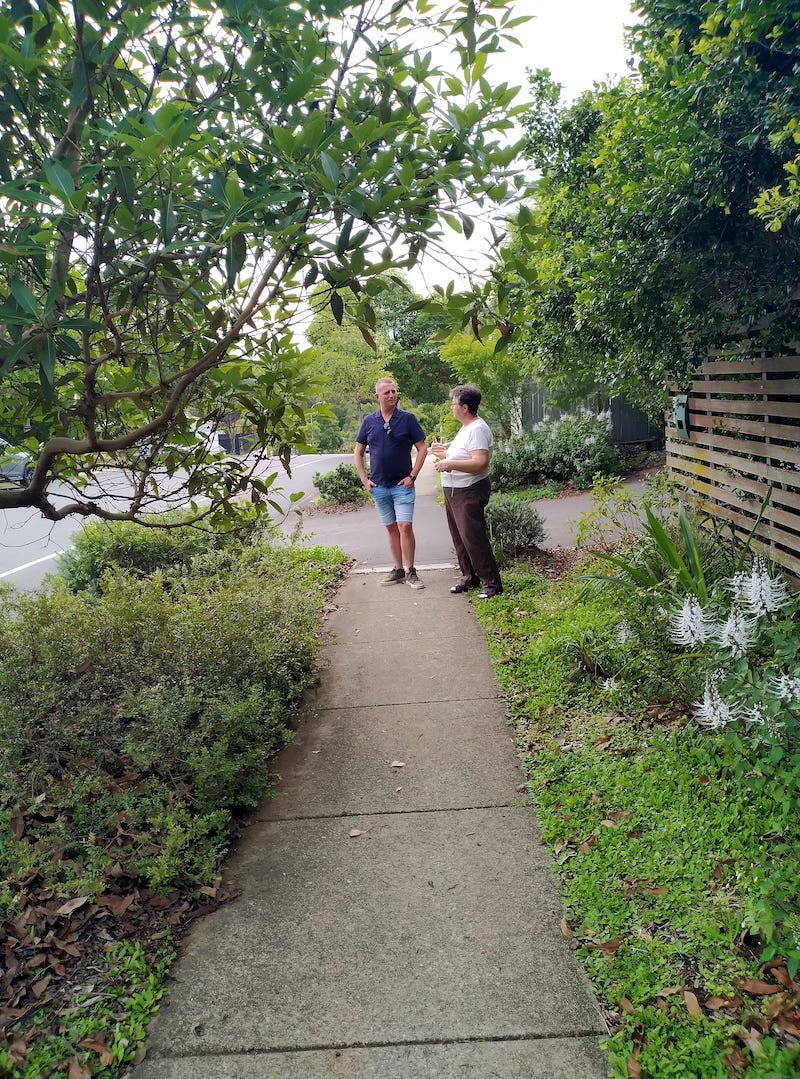 two people standing on a footpath with trees and garden both sides