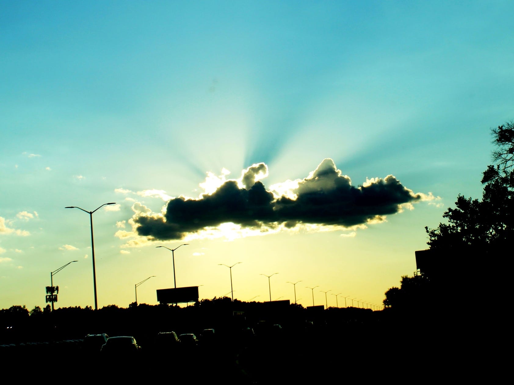 a cloud is backlit by the setting sun sky. The sky shifts from blue to turquoise to a greenish blue from the top to the bottom of the picture. 