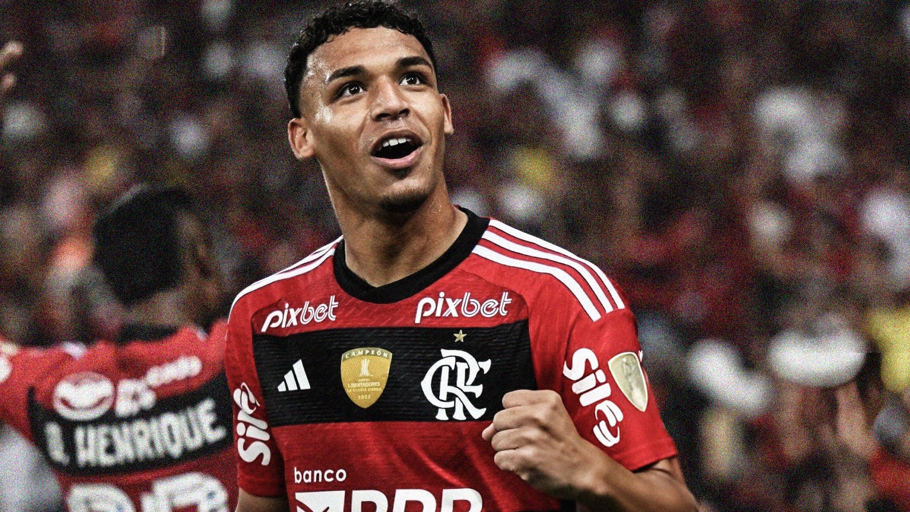 A close-up photo of Victor Hugo, looking high into the stadium with a clenched fist. He's wearing a red-and-black hooped Flamengo shirt.