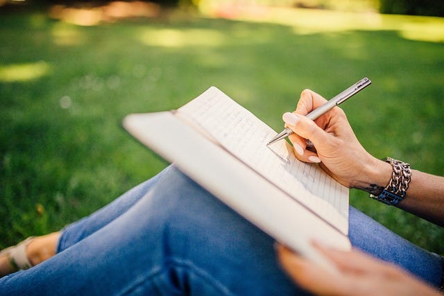 person writing with pen on journal propped against their knees