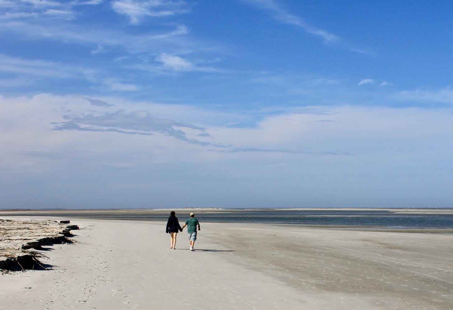 a man and woman walking hand in had on a beach with blue sky