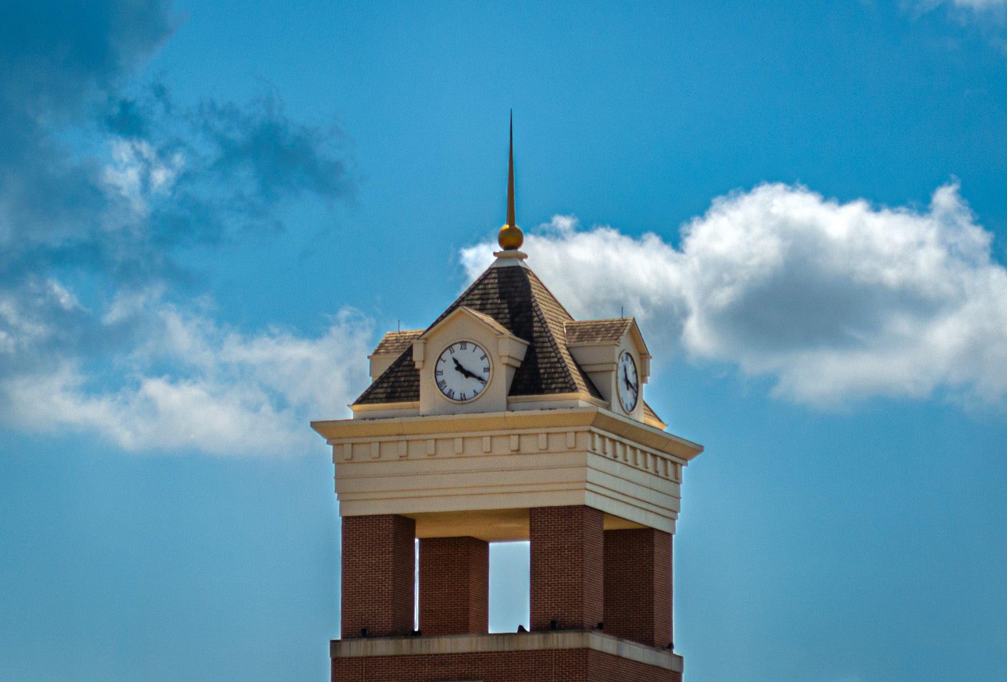 A clock tower showing the time, 11:20 am, against a blue sky with scattered white and grey clouds in the background
