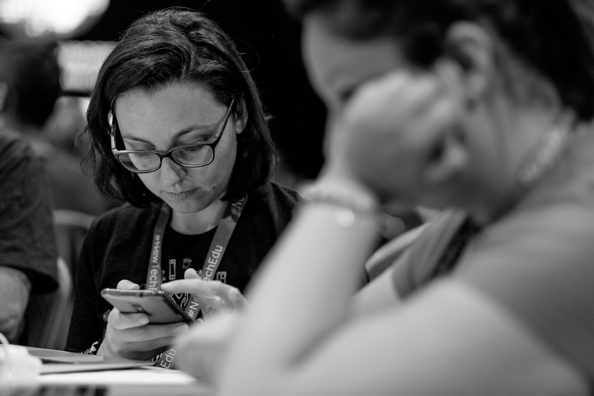 Una mia foto in bianco e nero scattata durante il WordCamp Europe 2018: tengo in mano il cellulare e ho lo sguardo rivolto verso lo schermo, si vedono soprattutto i miei enormi occhiali da vista.