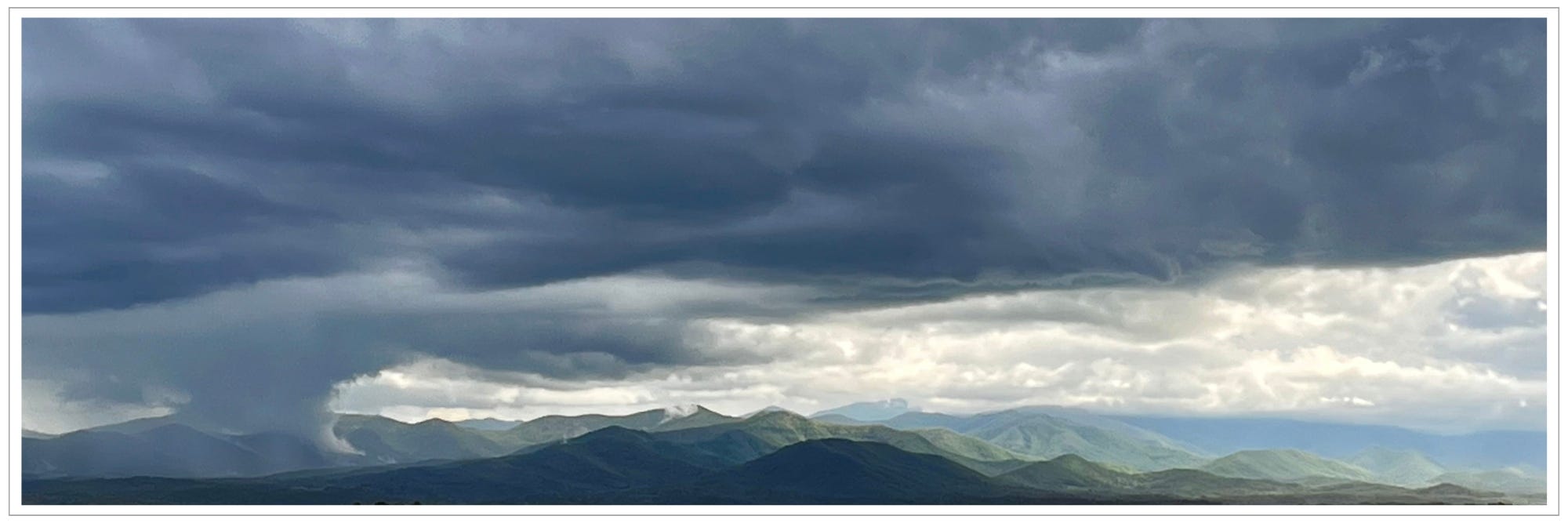 funnel shaped dark cloud hovering over and reaching into mountain ranges and valleys, greening ranges in the distance