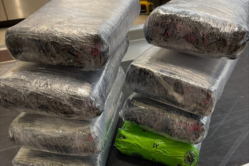 Packages wrapped in plastic are stacked in two columns on a grey bench.