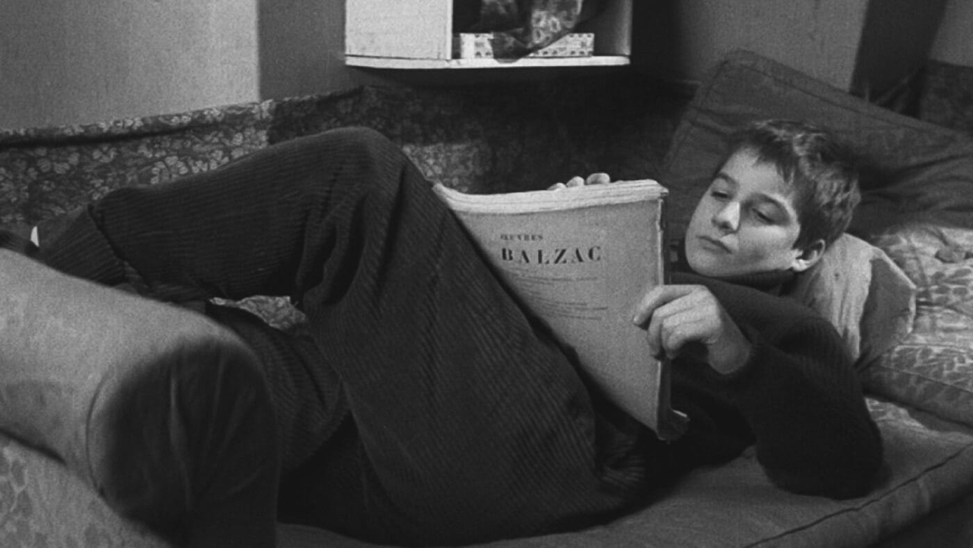 Antoine Doinel lounges on a couch reading a large Balzac book in a quiet domestic setting. Antoine Doinel lounges on a couch reading a large Balzac book in a quiet domestic setting.