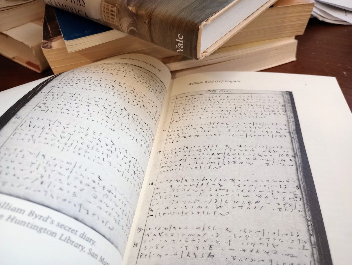 Open book on desk showing coded diary pages plus stack of books next to iy