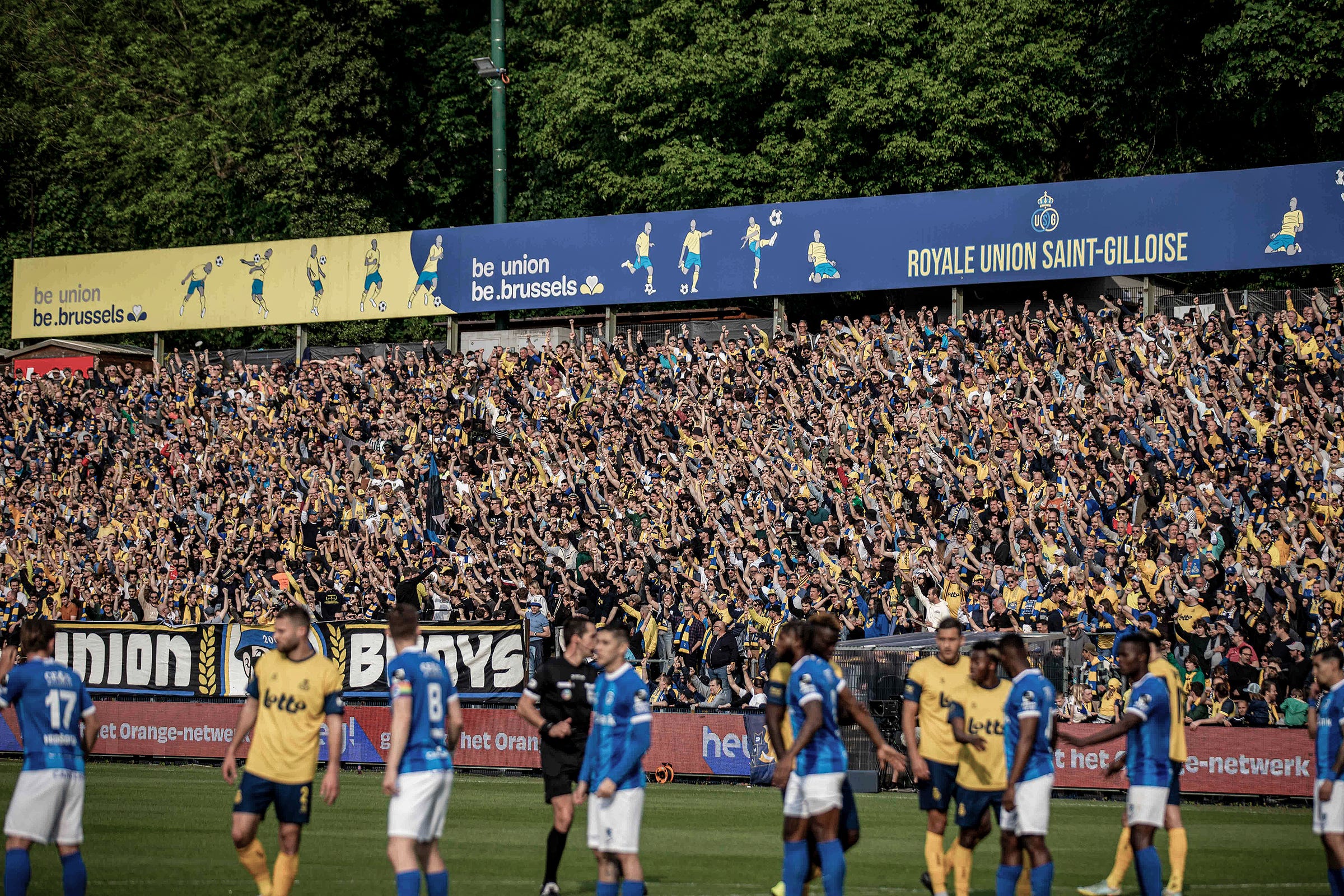 A photo of Royale Union Saint-Gilloise fans at the Stade Joseph-Marien with players in the foreground
