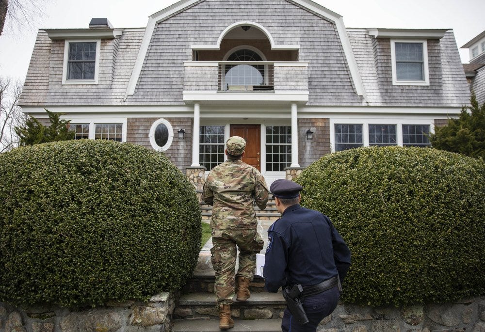 Rhode Island Air National Guard Tsgt. William Randall, left, and Westerly police officer Howard Mills approach a home while looking for New York license plates in driveways to inform them of self quarantine orders, Saturday, March 28, 2020, in Westerly, R.I. States are pulling back the welcome mat for travelers from the New York area, which is the epicenter of the country's coronavirus outbreak, and some say at least one state's measures are unconstitutional. Gov. Gina Raimondo ratcheted up the measures announcing she ordered the state National Guard to go door-to-door in coastal communities starting this weekend to find out whether any of the home's residents have recently arrived from New York and inform them of the quarantine order. (AP Photo/David Goldman)