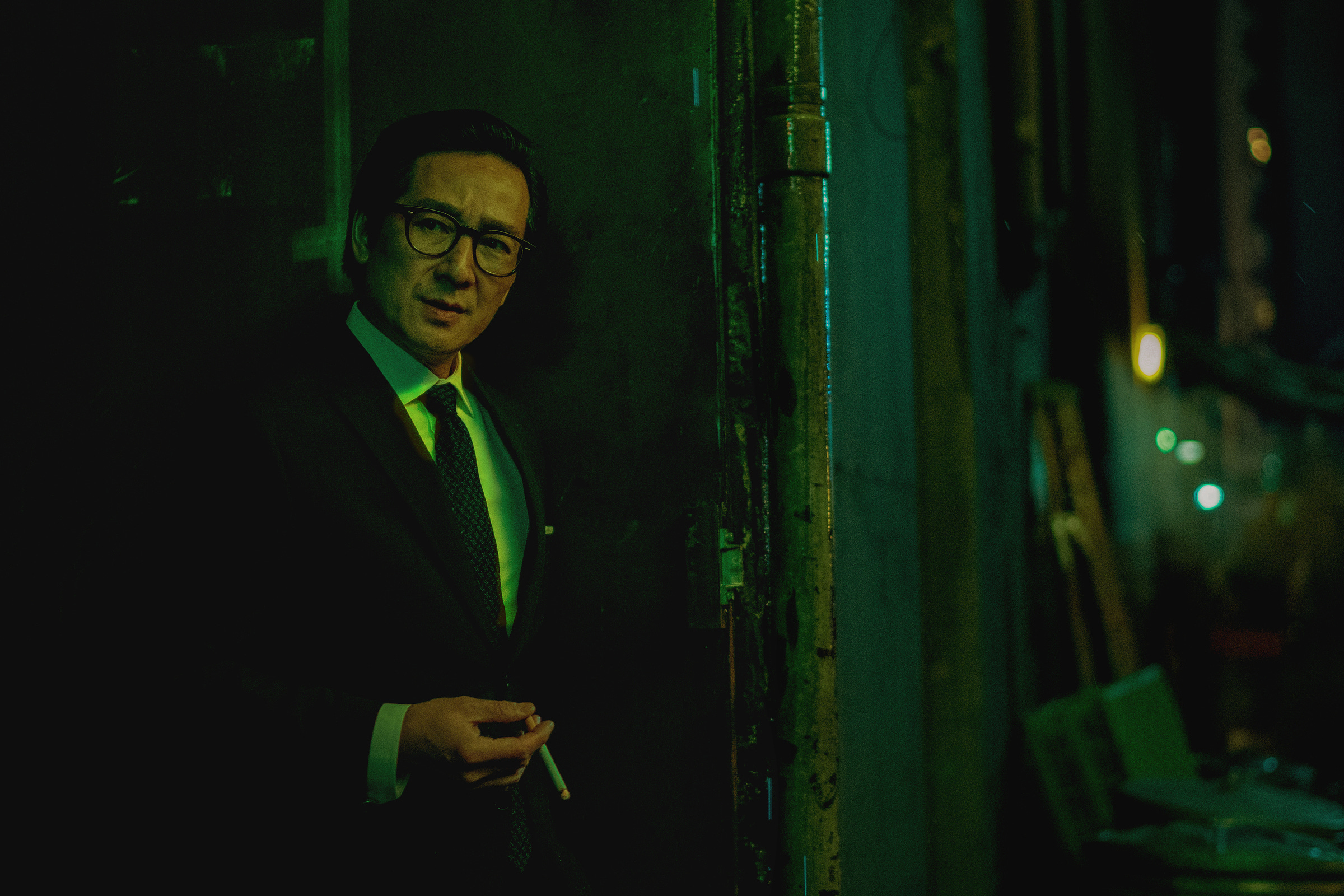 Ke Huy Quan stands in an alleyway in a suit with a cigarette in a scene from Everything Everywhere All At Once. The scene is an homage to Wong Kar-wai's In The Mood For Love