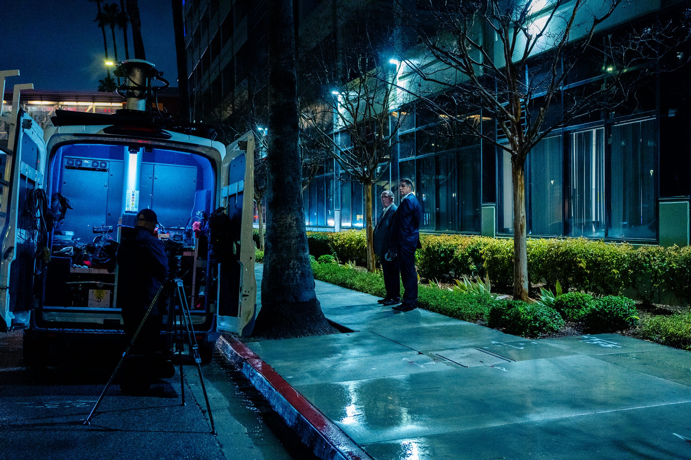 A news van is parked near two men in suits standing on an empty sidewalk