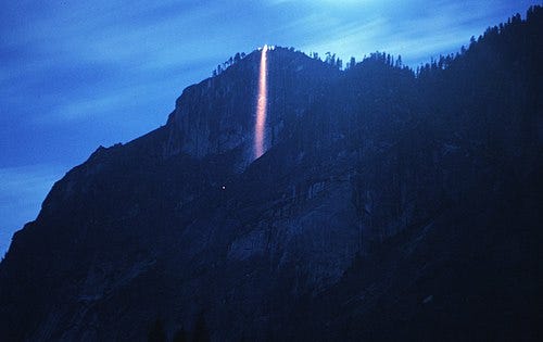 Long-exposure shot taken at distance of coals tumble over a cliff wall, appearing like a firey waterfall