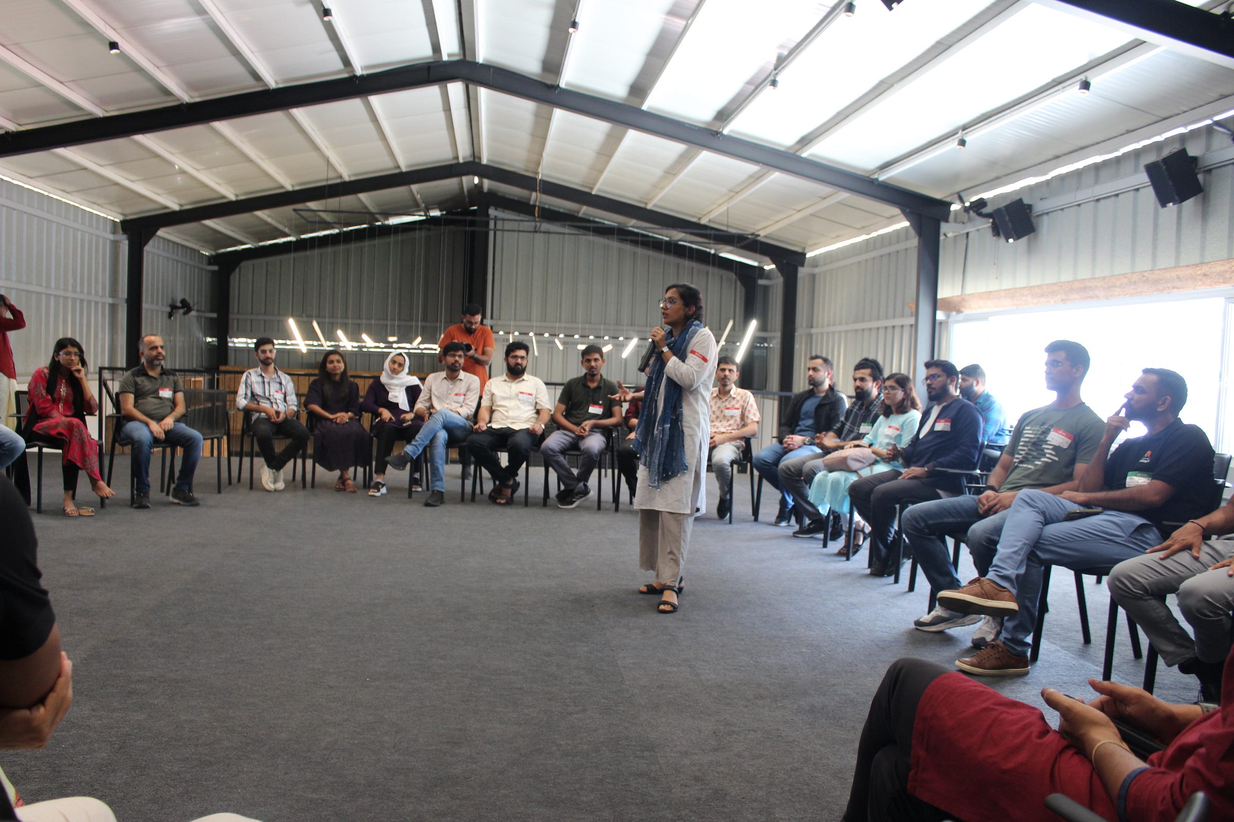 A group of people sitting in a circle, listening to a lady speak