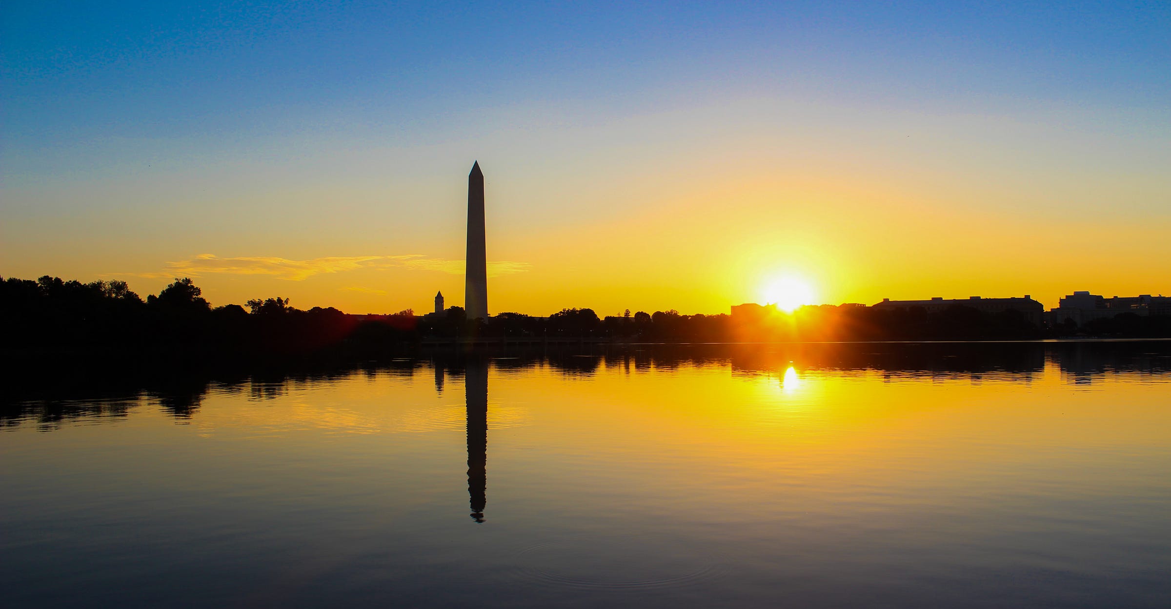 Photo of the sun coming up behind the Washington Monument and the Tidal Basin, in Washington D.C.