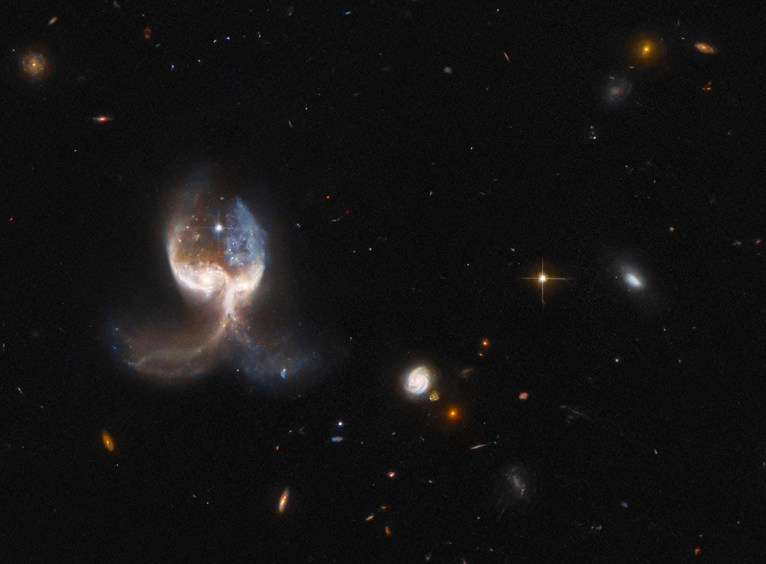 Hubble image of colliding galaxies that loosk like a slightly elongated bulbous head over a pair of curving tentacles, in a black background dotted with stars and a some smaller galaxies Hubble image of colliding galaxies that loosk like a slightly elongated bulbous head over a pair of curving tentacles, in a black background dotted with stars and a some smaller galaxies