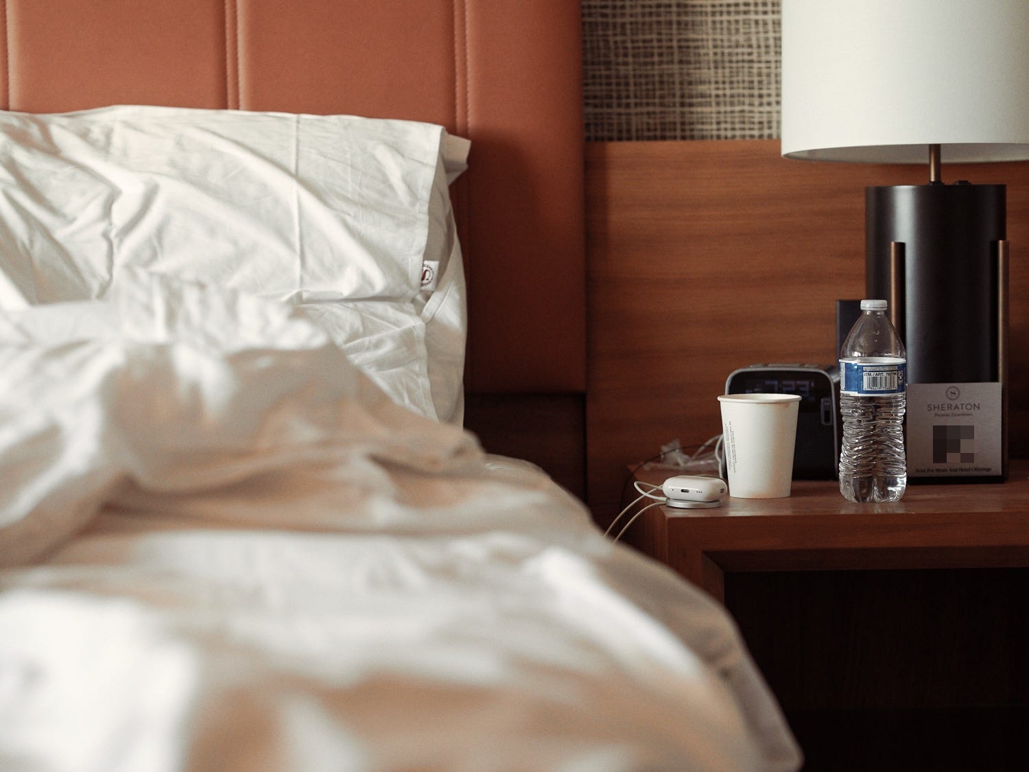 A used bed in a hotel room with a coffee and water nearby at the Sheraton in Phoenix AZ photographed by LA documentary photographer Afonso Salcedo