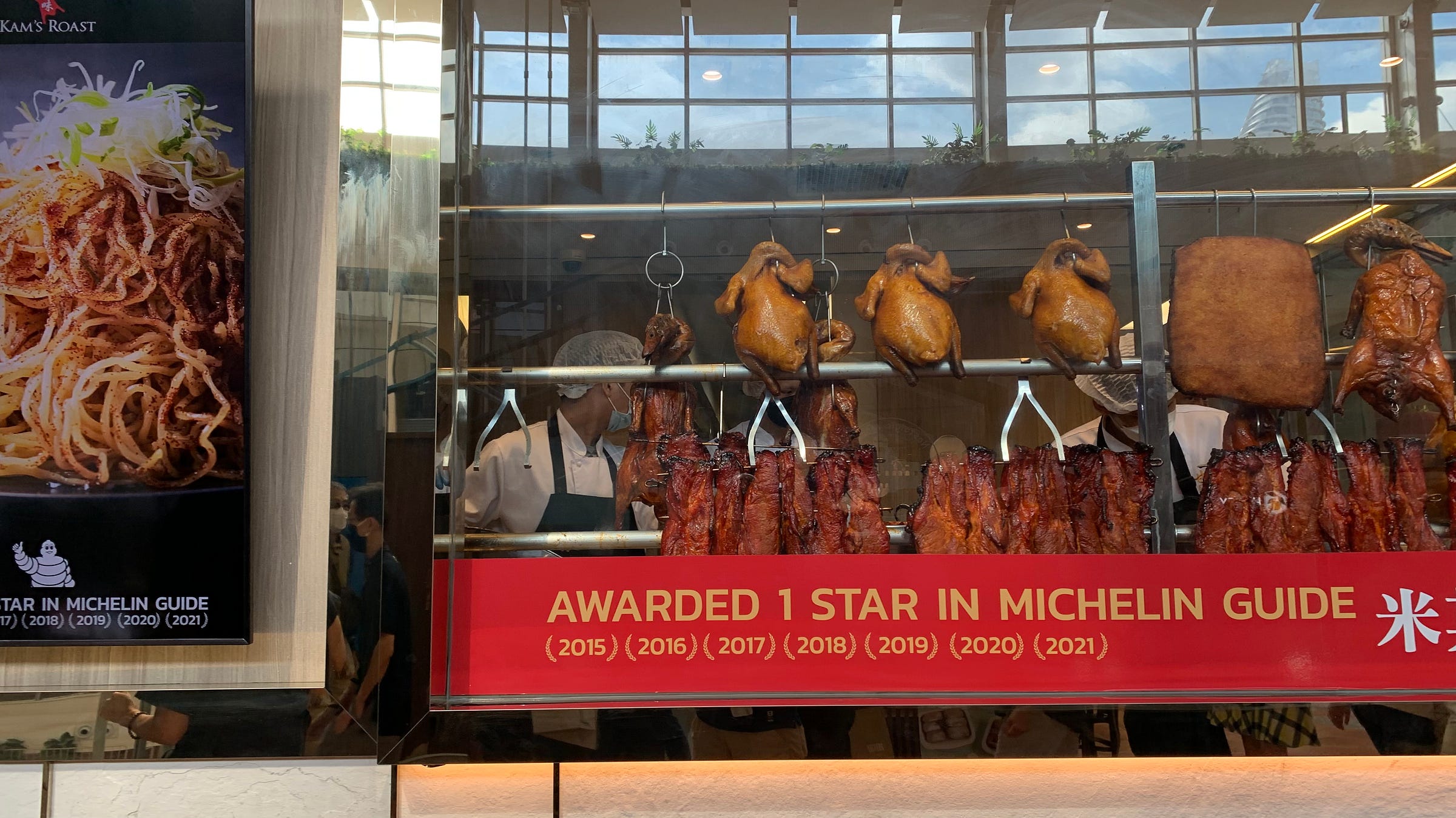View of roasted meats hanging in a restaurant window displaying consecutive years of 1 Michelin star.