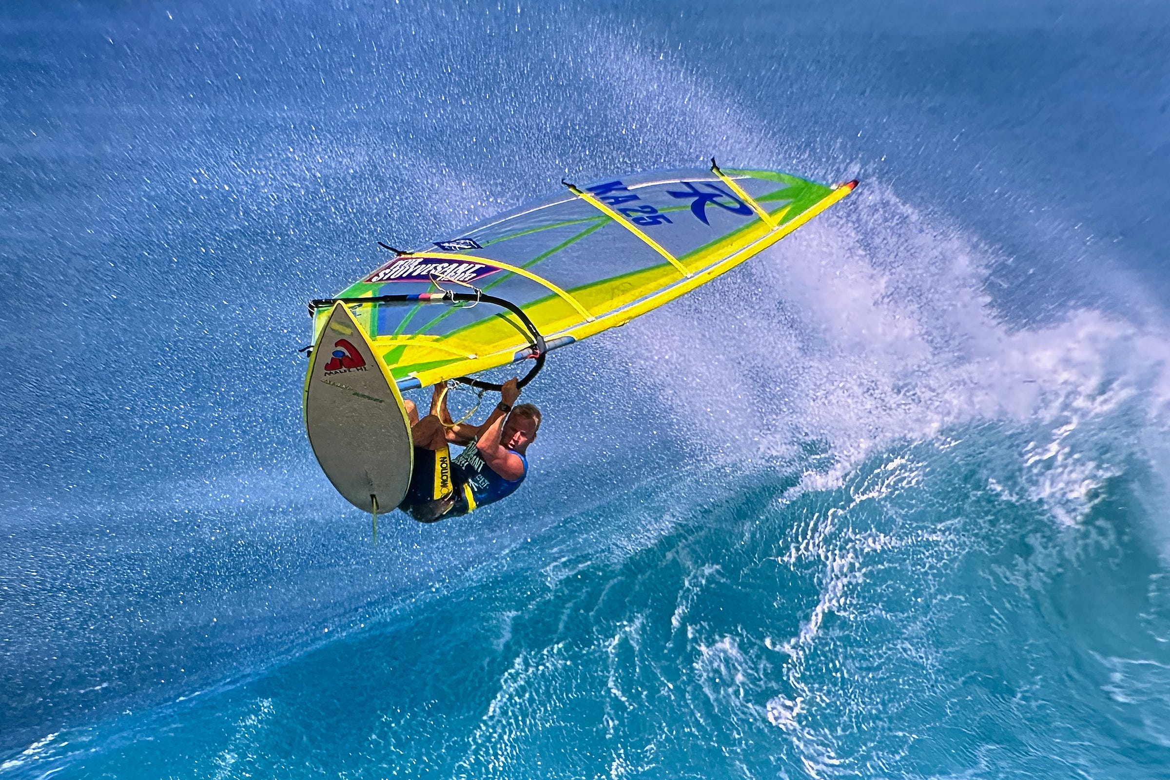 Photograph of a windsurfer on a white surf board with a bright yellow sail on a large wave in Hawaii.