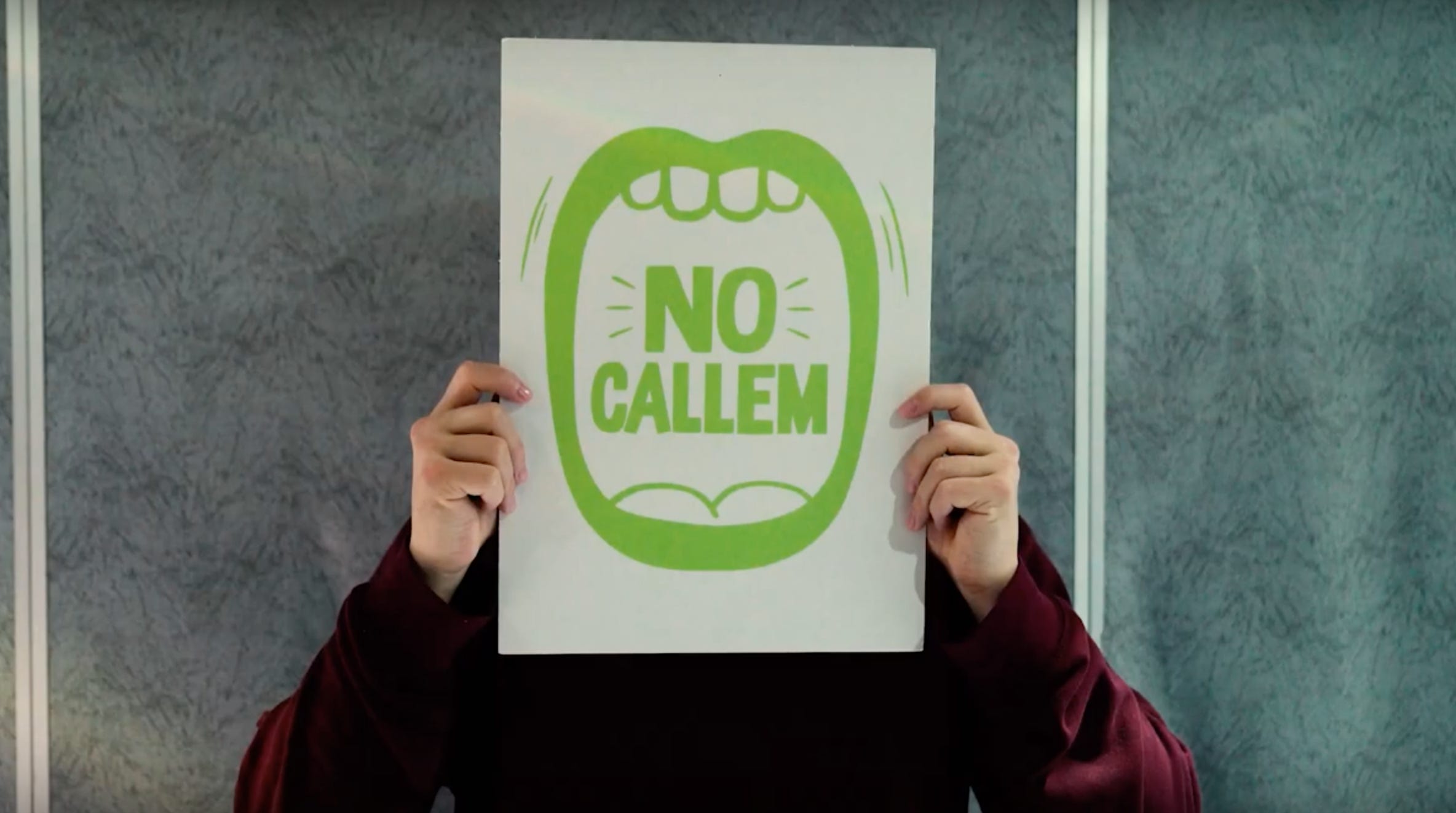 Schermata del video "Barcelona Ciutat Feminista" del comune di Barcellona: un cartello bianco con al centro l'illustrazione verde di una bocca spalancata e le parole NO CALLEM, non stiamo zitte.