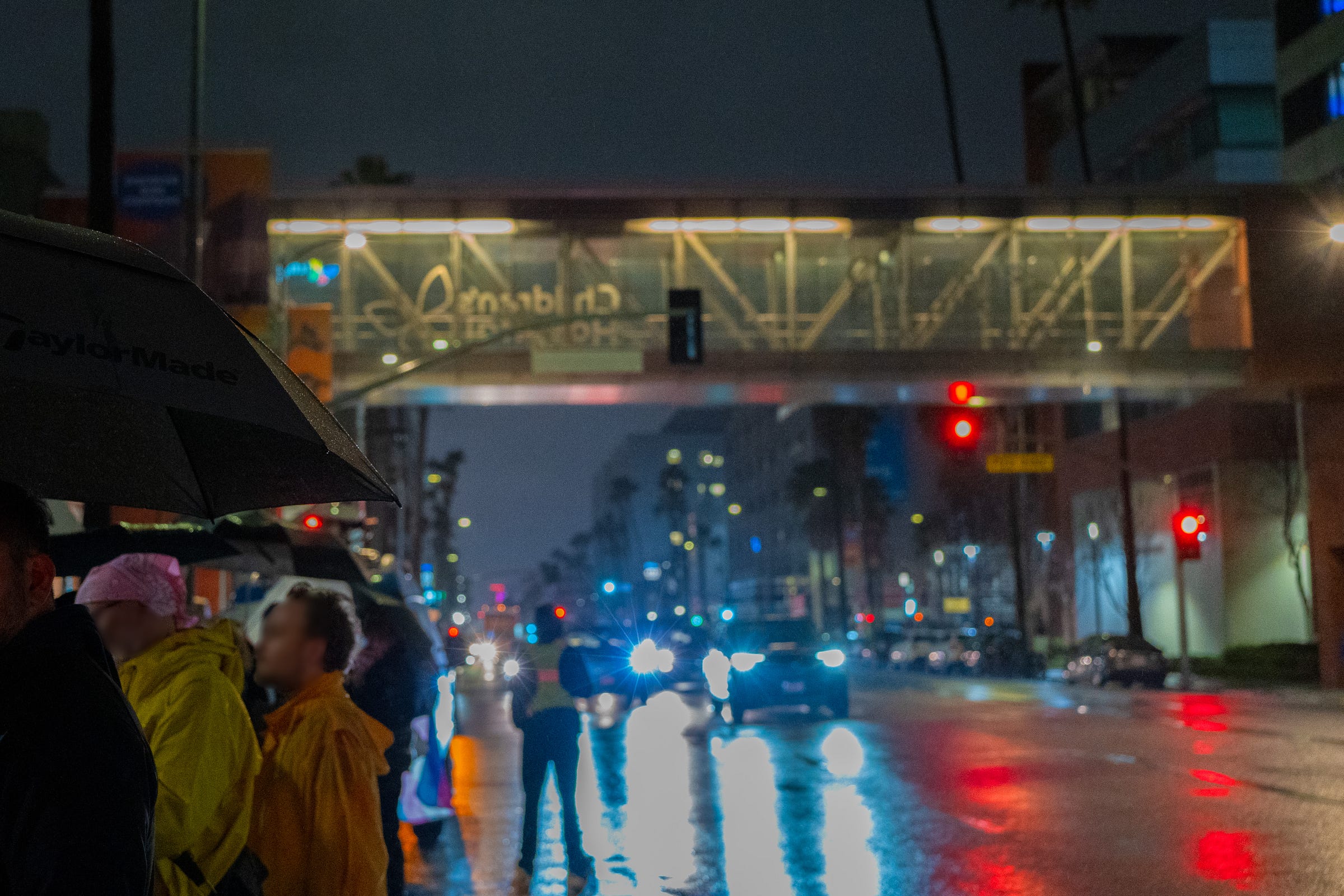 A pedestrian bridge over several cars and a person in a yellow vest standing in the road. A crowd of protestors with umbrellas huddles on the left side of the road.