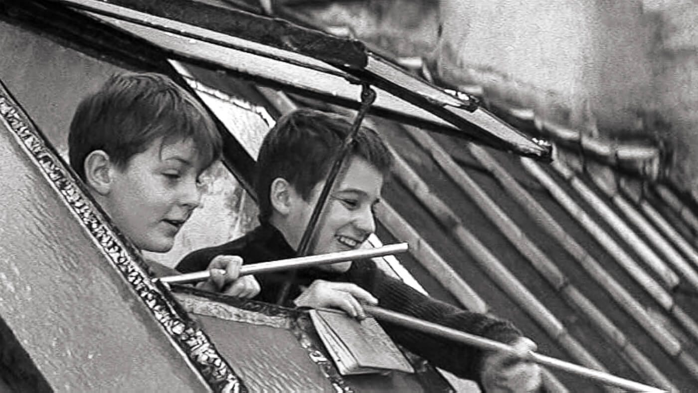 Antoine and another boy lean out a slanted rooftop window, laughing and launching spitballs using straws. Antoine and another boy lean out a slanted rooftop window, laughing and launching spitballs using straws.