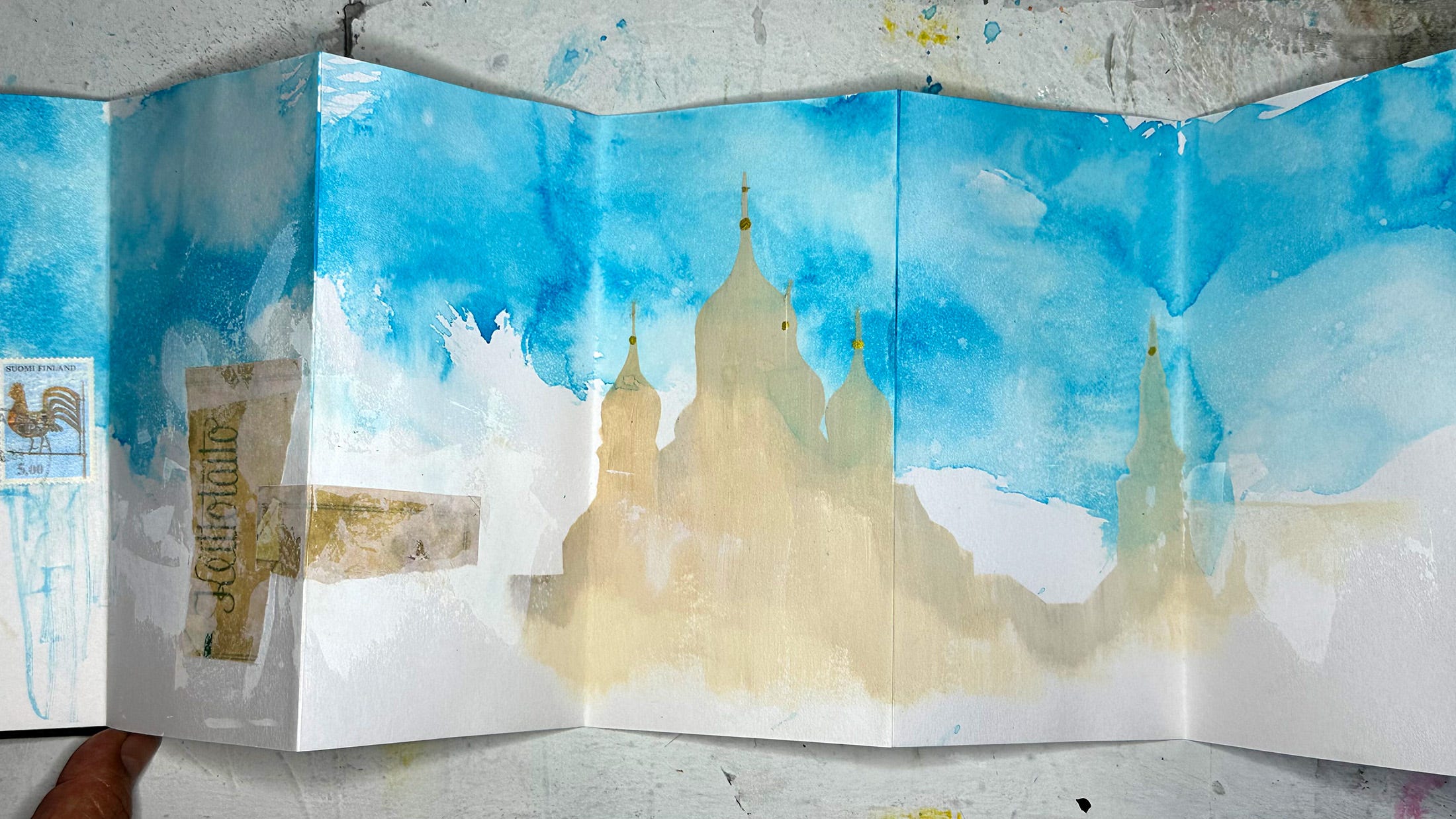 Pages in a concertina sketchbook showing blue ink wash in the 'sky' and a pale silhouette of a Russian cathedral in Estonia