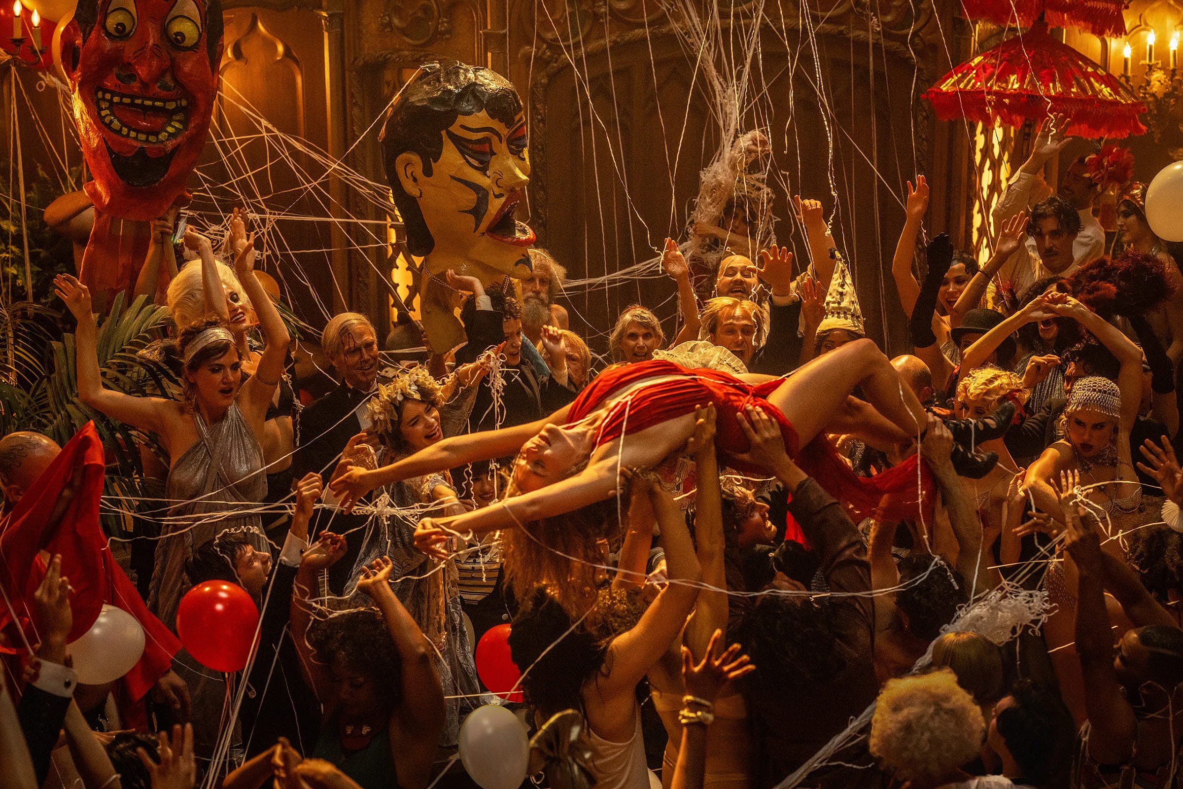 Margot Robbie as Nellie LaRoy, crowd surfing through a party in a red dress, and surrounded by revelers.