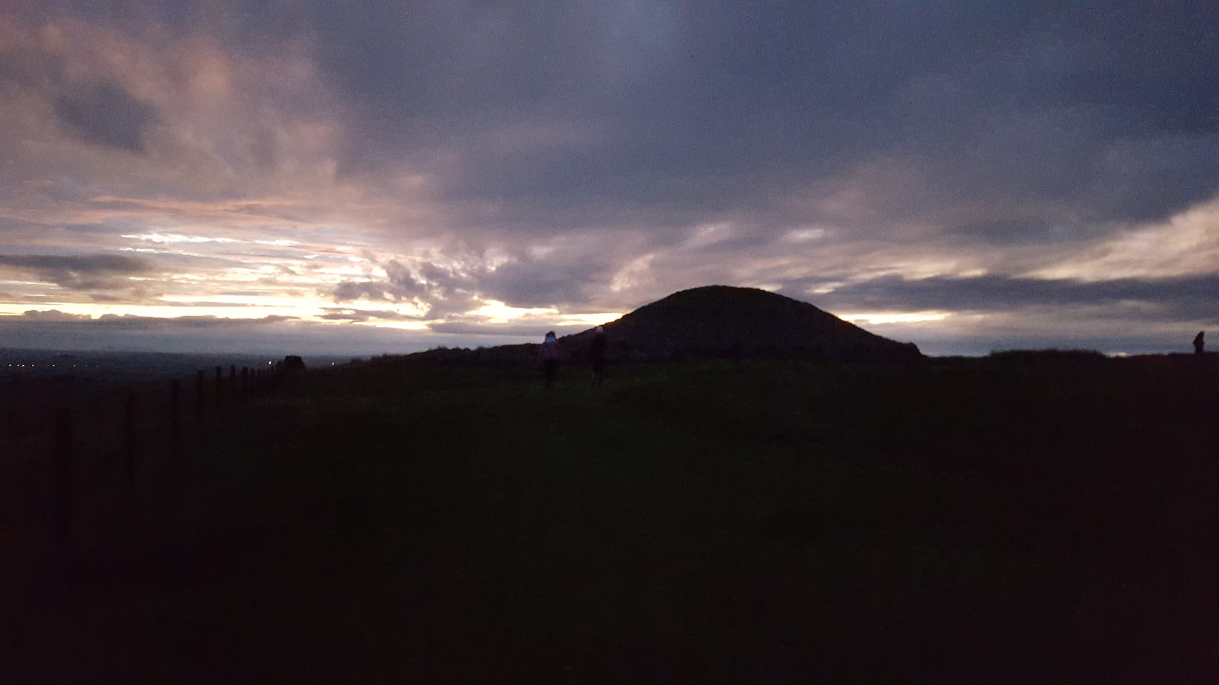 Black silhouette of cairn T, Loughcrew, against a purple sky as clouds begin to tear apart to reveal the rising sun, autumn equinox, 2015.