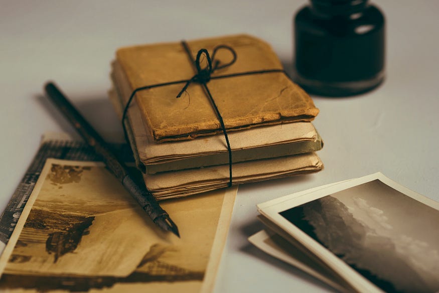 An image with a stack of old letters, bound by black string, and a pen next to it, on an old photograph.