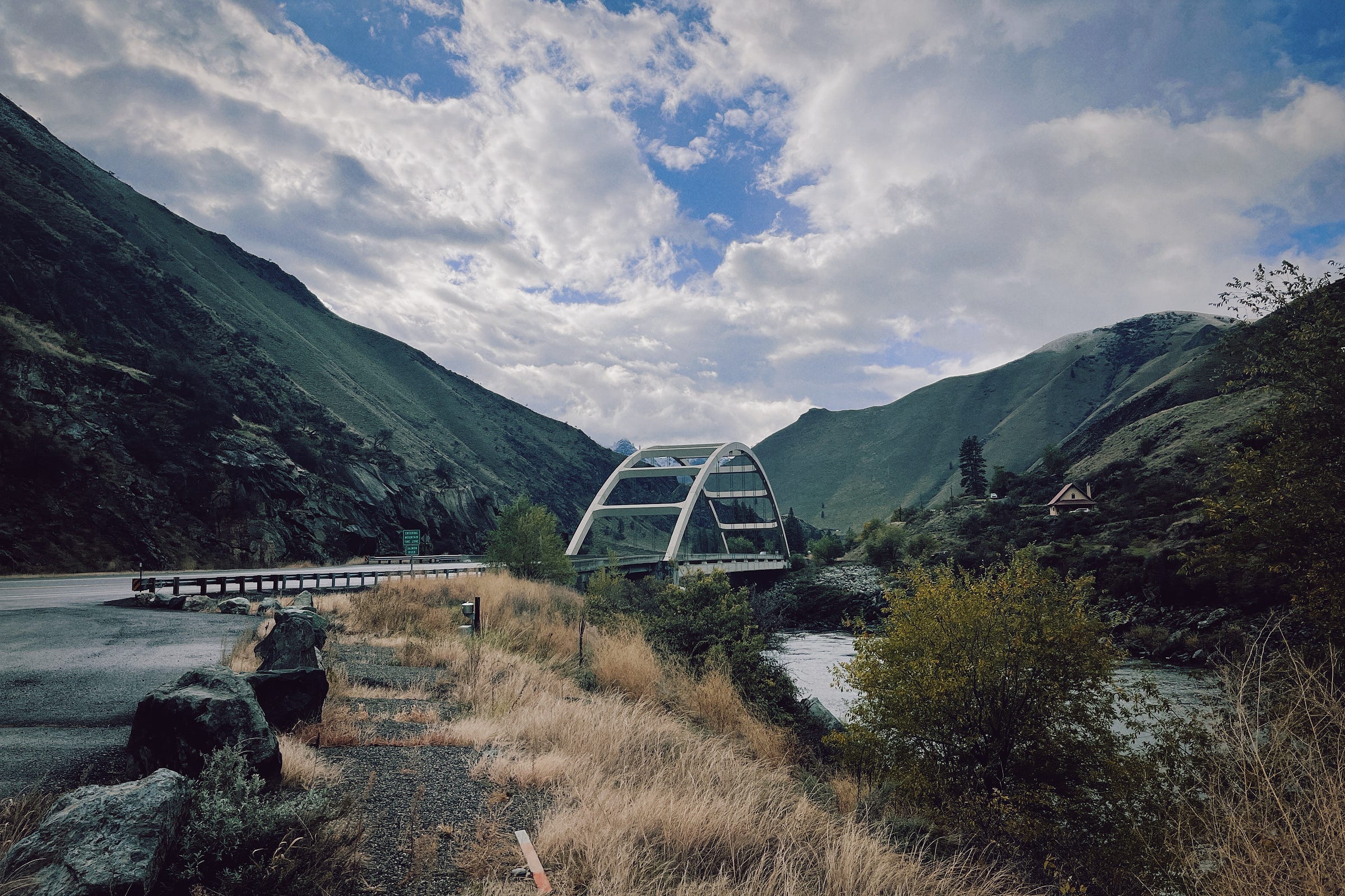 A photograph of Time Zone Bridge, a round-looking structure, with green mountains and blue skies in the background.