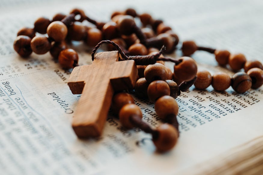 An image of a wooden cross on a rosary chain lying on a Bible.