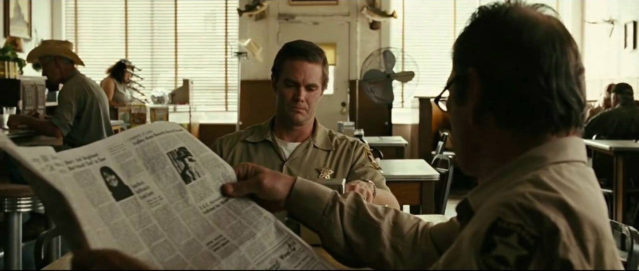 Escena de la película No es país para viejos en la que se ve dos hombres, uno de ellos sujeta un periódico