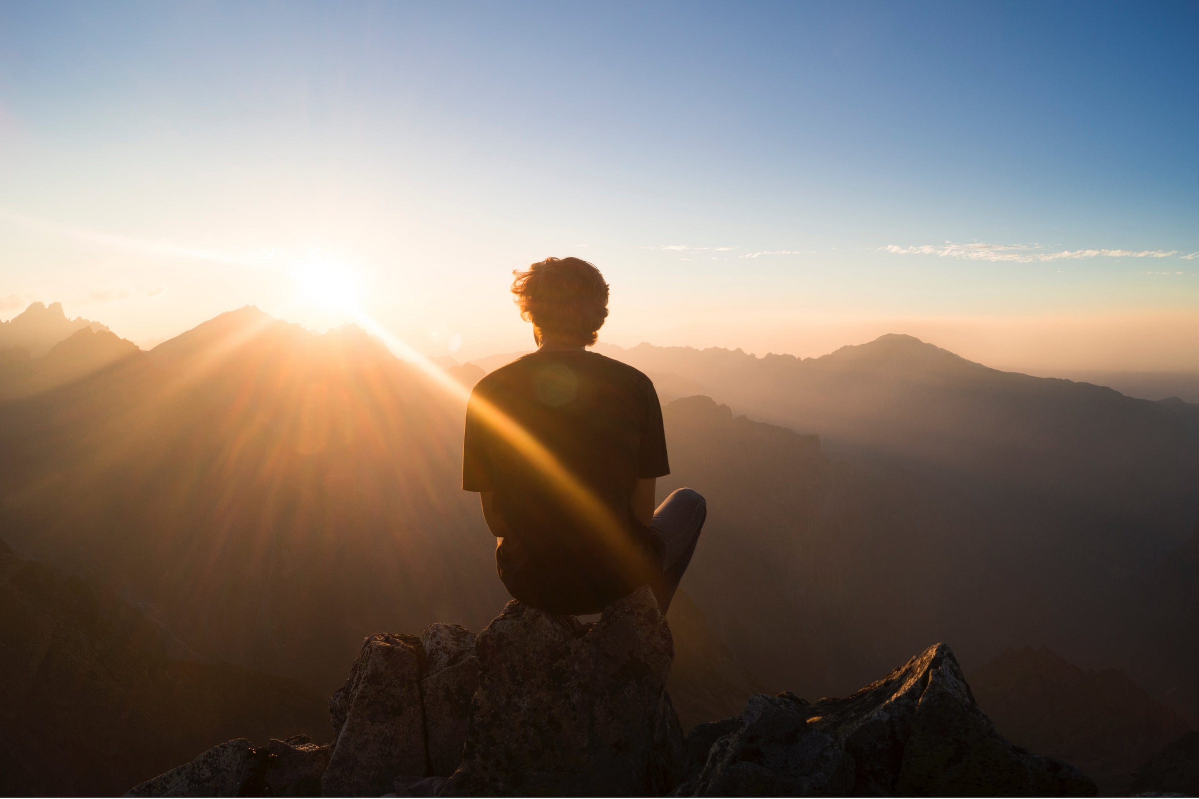 man sits on a mountain top watching a sunrise.