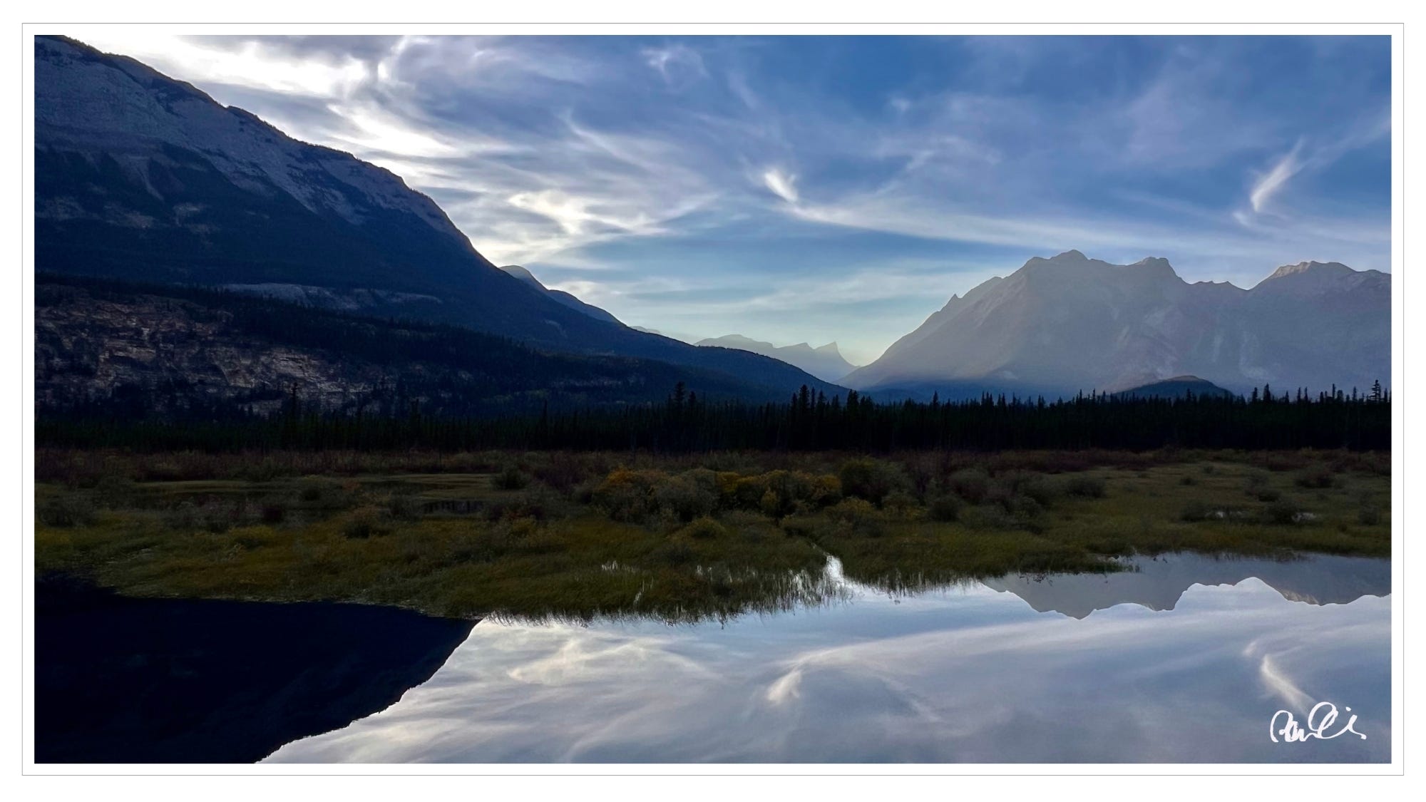 Glacier lake, water reflecting nearby mountains, clouds; Jasper National Park