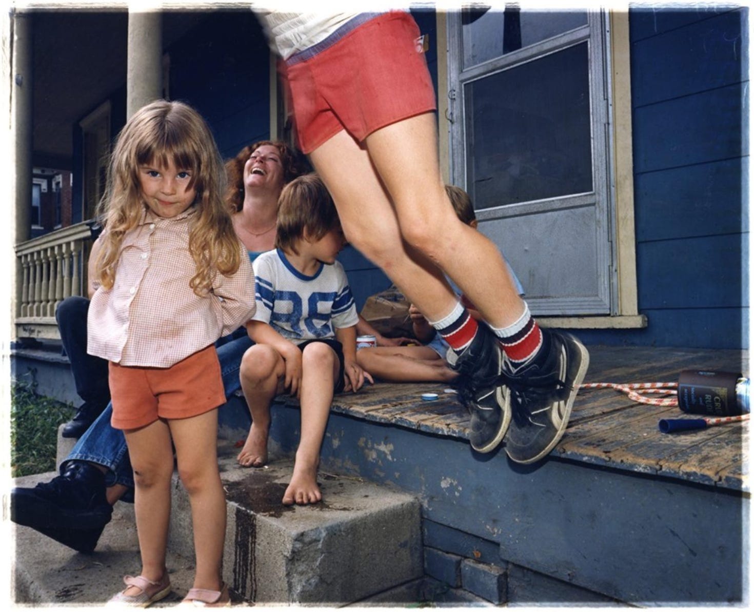 Four children play on a front porch while an adult sits next to them laughing Four children play on a front porch while an adult sits next to them laughing