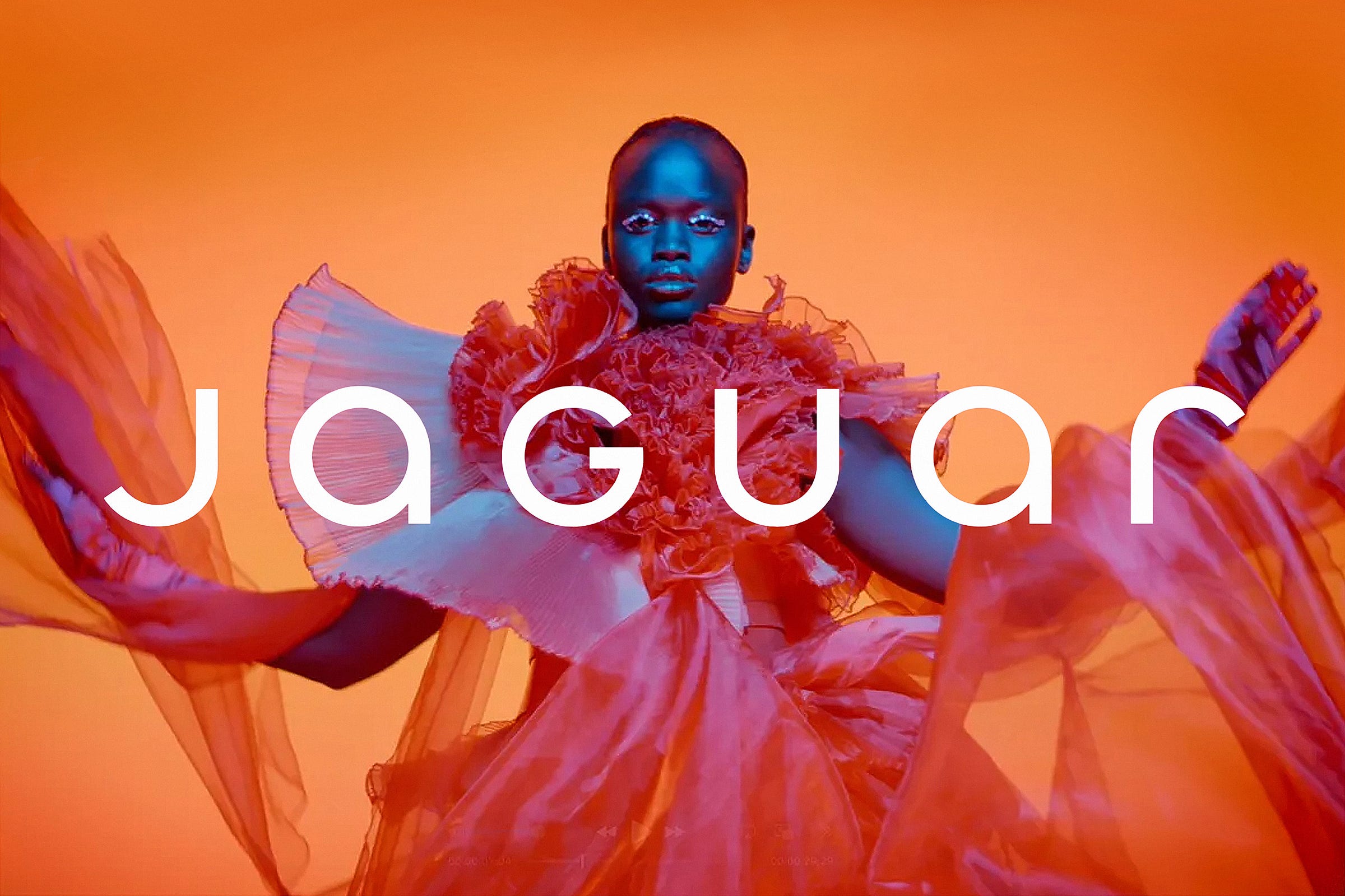 Photo of a Black model wearing a bright orange and magenta floating dress against a graded orange background with the word 'Jaguar' running across the center of the image.