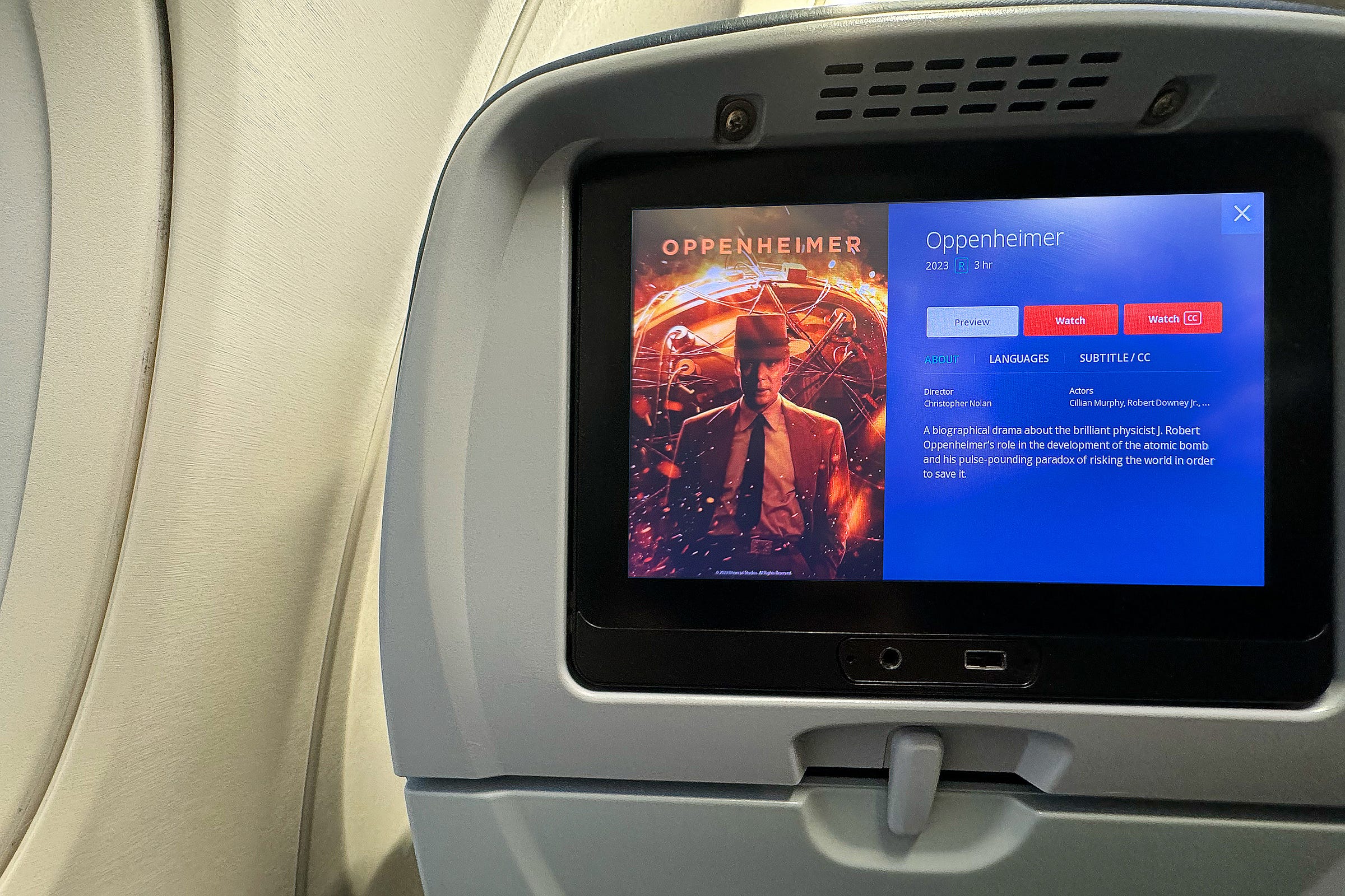 Photograph of an aircraft seatback with a video screen playing the movie 'Oppenheimer.'