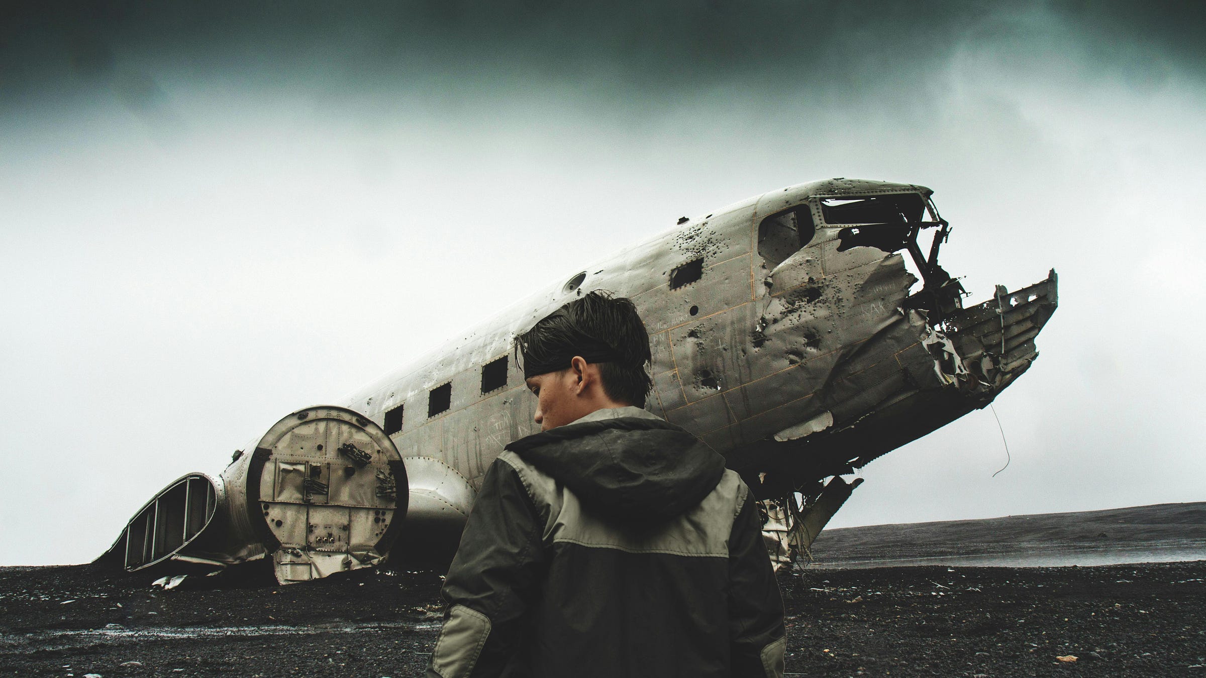 Man with a jacket with a hoodie in front of a crashed plane