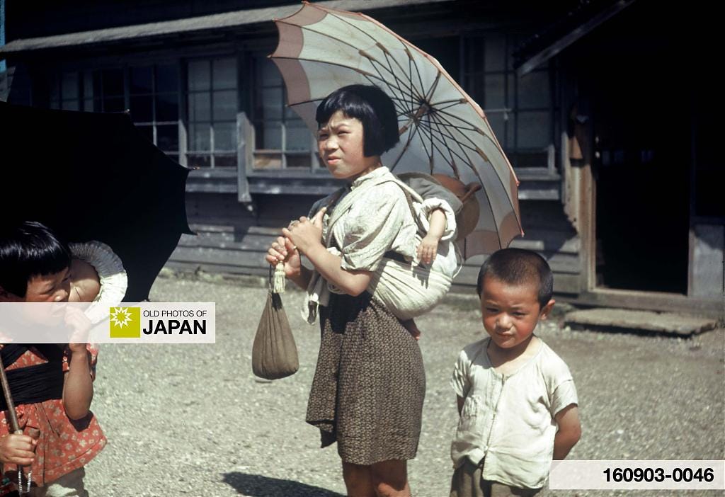 Young Japanese girls with umbrellas carrying babies, ca. 1950